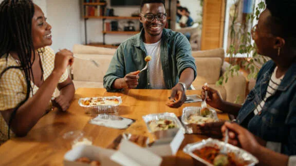 Young black friends eating take out food at home