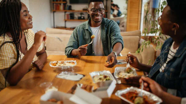 Young black friends eating take out food at home
